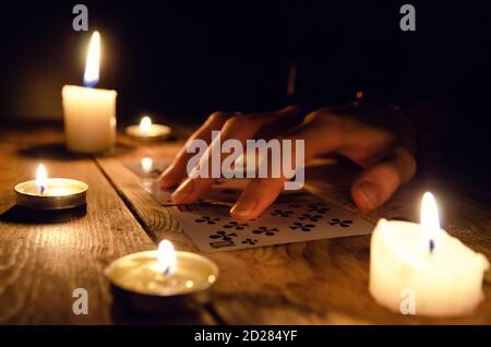 Hände eines Wahrsager und Karten auf dem Tisch, um brennende Kerzen im Dunkeln auf einem Holztisch. Konzept der Weissagung, Magie Stockfoto