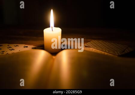 Mystische Atmosphäre, Karten, ein Buch, eine brennende Kerze im Dunkeln auf einem Holztisch. Esoterisches Konzept, Wahrsagen und Vorhersagen Stockfoto