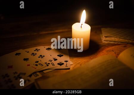 Mystische Atmosphäre, Karten, ein Buch, eine brennende Kerze im Dunkeln auf einem Holztisch. Esoterisches Konzept, Wahrsagen und Vorhersagen Stockfoto