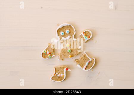 Lebkuchenmann mit abgetrennten Beinen und Armen. Die Gliedmaßen des Keks sind vom Körper getrennt. Weihnachts-Lebkuchen auf weißem Holzhintergrund. Stockfoto