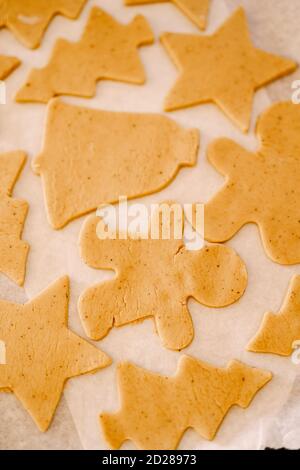 Prozess der Herstellung von hausgemachten Cookies oder Lebkuchen in verschiedenen Formen. Rohe Teigkekse liegen auf einem mit Pergament überzogenen Backblech zum Backen vor Stockfoto