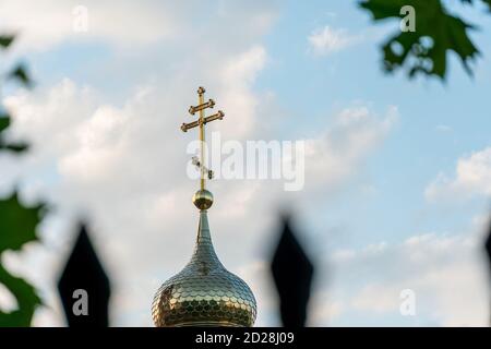 Kuppel der orthodoxen Kirche mit einem Kreuz Nahaufnahme durch Birkenzweige gegen den blauen Himmel. Orthodoxes Kreuz Stockfoto