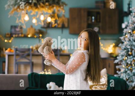 Ein Mädchen hält einen ausgestopften Hasen in der Nähe eines Weihnachtsbaums. Geschenke werden um den geschmückten Weihnachtsbaum zu Hause platziert. Stockfoto