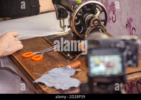 Alte Vintage Nähmaschine Nahaufnahme. Blogger auf Kamera mit Stativ schießt einen Bericht über das Nähgeschäft Stockfoto