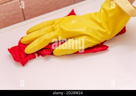 Weibliche Hand in einem gelben Handschuh mit einem roten Lappen wäscht die weiße Oberfläche der Waschmaschine. Das Zimmermädchen putzt das Haus. Stockfoto