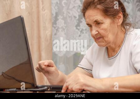 Ältere dunkelhaarige Frau sitzt an einem Tisch mit einem schwarzen Laptop und schaut auf den Monitor Stockfoto