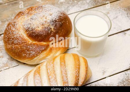 Glas Milch, Laib, auf einem hölzernen Hintergrund mit Mehl. Ausgewogene Ernährung, Eiweiß und Kohlenhydrate, Getreide Stockfoto