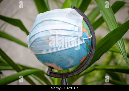 Globus in einer medizinischen Maske zwischen den Blättern der Pflanzen. Globale Pandemie covid-19, Coronavirus. Konzept der Ausbreitung des Virus Stockfoto