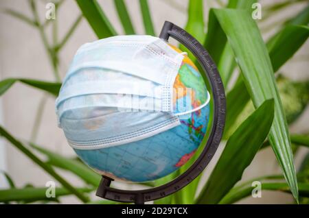 Globus in einer medizinischen Maske zwischen den Blättern der Pflanzen. Globale Pandemie covid-19, Coronavirus. Konzept der Ausbreitung des Virus Stockfoto