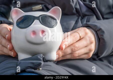 Mädchen in einer Jacke hält eine rosa Sparschwein Bank mit Brille auf dem Schoß aus nächster Nähe Stockfoto