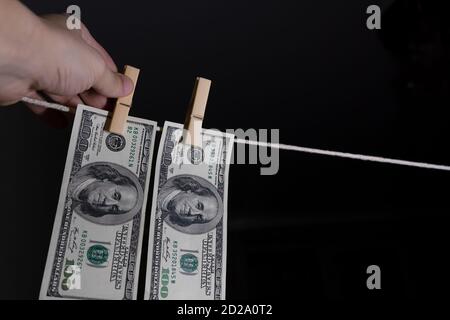 Die Hand des Mannes hängt Dollar auf einem schwarzen Hintergrund mit Wäscheklammern an einem Seil. Konzept des schmutzigen Geldes. Stockfoto