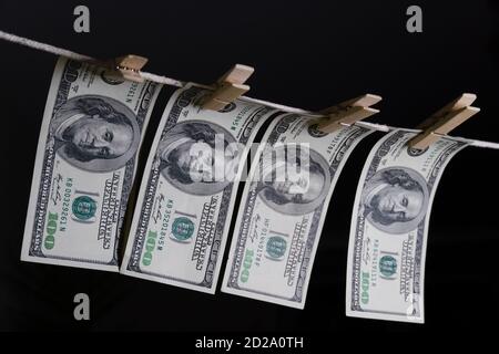 Einhundert Dollarscheine hängen mit Wäscheklammern auf einer Schnur auf schwarzem Hintergrund. Konzept des schmutzigen Geldes. Dollar fällt. Stockfoto