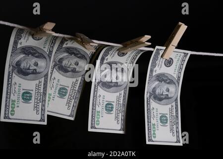 Einhundert Dollarscheine hängen mit Wäscheklammern auf einer Schnur auf schwarzem Hintergrund. Konzept des schmutzigen Geldes. Dollar fällt. Stockfoto