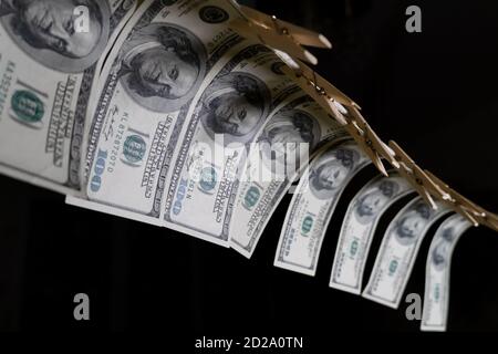 Einhundert Dollarscheine hängen mit Wäscheklammern auf einer Schnur auf schwarzem Hintergrund. Konzept des schmutzigen Geldes. Dollar fällt. Stockfoto