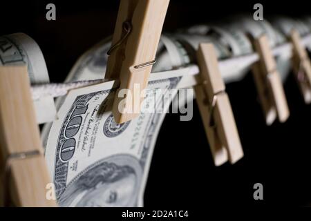 Einhundert Dollarscheine hängen mit Wäscheklammern auf einer Schnur auf schwarzem Hintergrund. Konzept des schmutzigen Geldes. Dollar fällt, Nahaufnahme Stockfoto