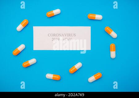 Weißes Blatt Papier mit der Aufschrift Coronavirus zwischen orangen und weißen Kapseln auf blauem Hintergrund. Medizinischer Hintergrund, Draufsicht Stockfoto