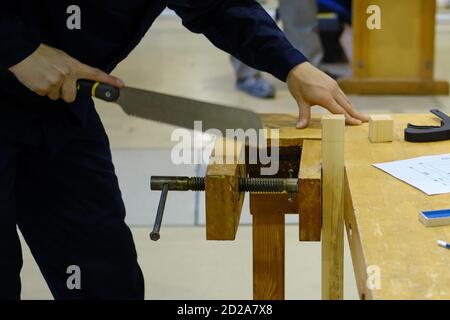 Ein Zimmermann schneidet ein Stück einer Bar mit einem Hacksäge auf einer hölzernen Werkbank Stockfoto