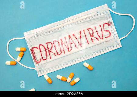 Medizinische Maske mit der Inschrift Coronavirus und verstreut orange und Weiße Kapseln auf blauem Hintergrund mit einem Kopierplatz Stockfoto