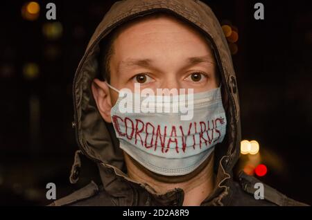 Mann in einer Haube mit einer medizinischen Maske auf seinem Gesicht mit der Inschrift Coronavirus im Dunkeln. Konzept der Gesundheitsversorgung, Medizin Stockfoto