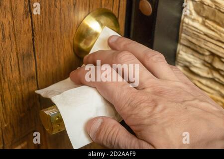 Die Hand des Mannes greift mit einer weißen Serviette an den Türgriff. Eine notwendige Methode zur Verhinderung des verbreiteten Coronavirus Stockfoto