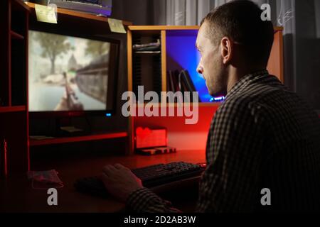 Seitenansicht eines fokussierten jungen Mannes, der bei einem spielt Computer im Dunkeln Stockfoto
