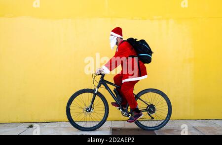 Kaukasischer Mann trägt Weihnachtsmann Kleidung und Fahrrad fahren mit Eine gelbe Wand auf dem Hintergrund Stockfoto
