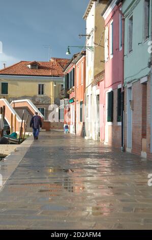 Venedig-Insel Burano, Blick auf eine Straße im Nachmittagslicht, heller und dunkler Himmel nach einem Sturm, traditionelle venezianische bemalte Fassaden Stockfoto