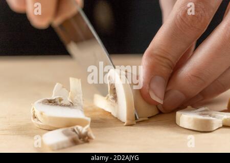 Frauenhände schneiden Pilze aus nächster Nähe auf einem Holzbrett Stockfoto