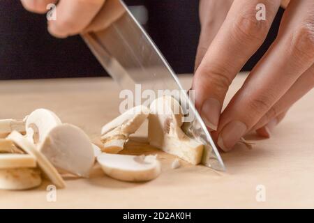 Frauenhände schneiden Pilze aus nächster Nähe auf einem Holzbrett Stockfoto