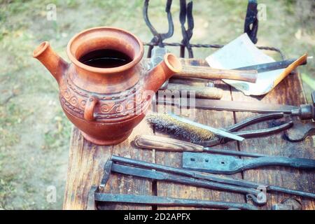 Retro Schmied Werkzeuge auf Holztisch in Schmiede. Krug zum Härten von Eisen, Zangen und anderen Werkzeugen zum Schmieden. Stockfoto