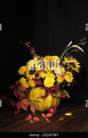 Blumenarrangement mit Sonnenblumen in einem Kürbis auf schwarzem Hintergrund. Thanksgiving und Copy Space Konzept Stockfoto