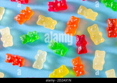 Köstliche helle bunte Gelee Bären auf einem blauen Hintergrund zufällig mit harten Schatten verstreut, Draufsicht Stockfoto