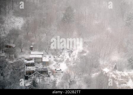 Schneesturm im Wald über einem zerstörten Holzhaus. Schneesturm mit Schnee im Winterwald, Draufsicht Stockfoto