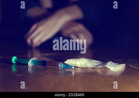 Spritze und Drogen mit einem defocused Mann sitzt auf dem Boden und seine Hände. Konzept der sucht. Getöntes Foto Stockfoto