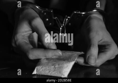 Hände mit Handschellen, die einen Beutel mit Drogen in der Nähe halten. Schwarzweiß-Foto Stockfoto