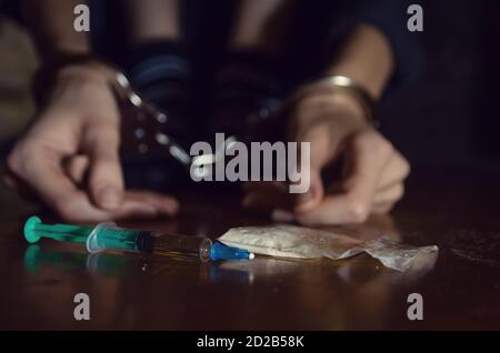 Spritze und Drogen mit einem entkokelten Mann auf dem Boden sitzen und seine Hände in Handschellen gesperrt.Addict. Stockfoto