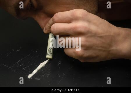 Männliche Hände schnüffeln Drogen durch einen Dollar auf einem schwarzen Nahaufnahme des Hintergrunds Stockfoto