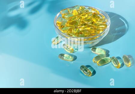 Gelatine transparente Kapseln mit Fischöl in einer Glasschüssel auf blauem Hintergrund. Stockfoto