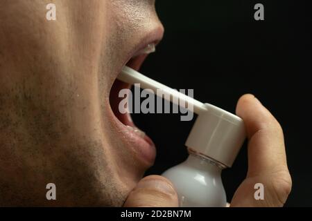 Porträt eines Mannes mit Kehlspray auf einem schwarzen Hintergrund Nahaufnahme, Kopierraum Stockfoto