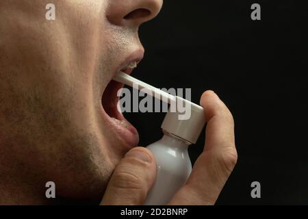 Porträt eines Mannes mit Kehlspray auf einem schwarzen Hintergrund Nahaufnahme, Kopierraum Stockfoto