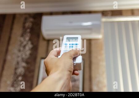 Nahaufnahme der Hand eines Mannes mit einer Fernbedienung gerichtet An der Klimaanlage an einer dunklen Wand Stockfoto