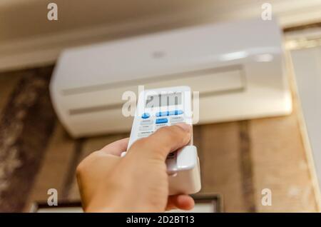 Nahaufnahme der Hand eines Mannes mit einer Fernbedienung gerichtet An der Klimaanlage an einer dunklen Wand Stockfoto