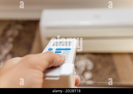 Nahaufnahme der Hand eines Mannes mit einer Fernbedienung gerichtet An der Klimaanlage an einer dunklen Wand Stockfoto