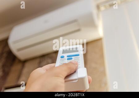 Nahaufnahme der Hand eines Mannes mit einer Fernbedienung gerichtet An der Klimaanlage an einer dunklen Wand Stockfoto