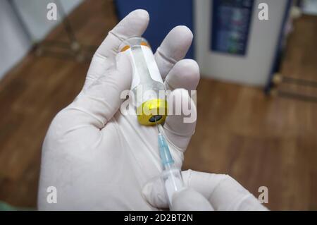 Doktor Füll Spritze mit Medikamenten, Nahaufnahme. Sichtbare Hände in weißen Handschuhen, Ampulle und Teil einer Spritze. Impfungen und Impfungen Stockfoto