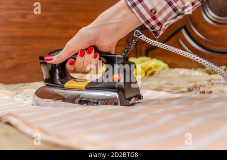 Nahaufnahme der Hand einer Frau mit rotem Nagellack mit Ein altes Eisen, das ein gestreiftes T-Shirt bügelt Stockfoto