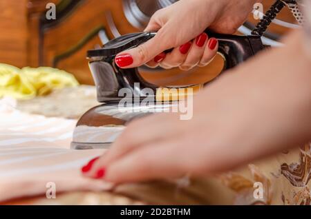 Nahaufnahme der Hand einer Frau mit rotem Nagellack mit Ein altes Eisen, das ein gestreiftes T-Shirt bügelt Stockfoto