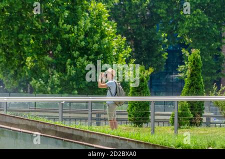 Fotografie oder das Konzept des Reisenden. Mann Reisende in Shorts, T-Shirt, Hut und Rucksack fotografieren in der Stadt an einem sonnigen Tag Stockfoto