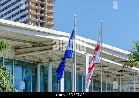 Flagge der Europäischen Union und Georgiens auf dem Hintergrund eines Glasgebäudes, ein Baum Stockfoto