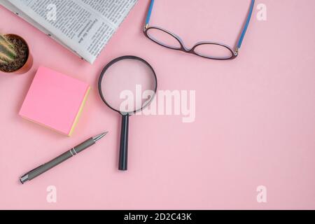 Flach legen auf einem rosa Hintergrund von Gläsern, Lupe, Gadget, Kaktus, Stift und Morgenzeitung Stockfoto